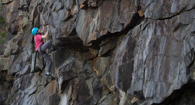 A person wearing safety gear is secured by ropes as they climb a rock wall. 